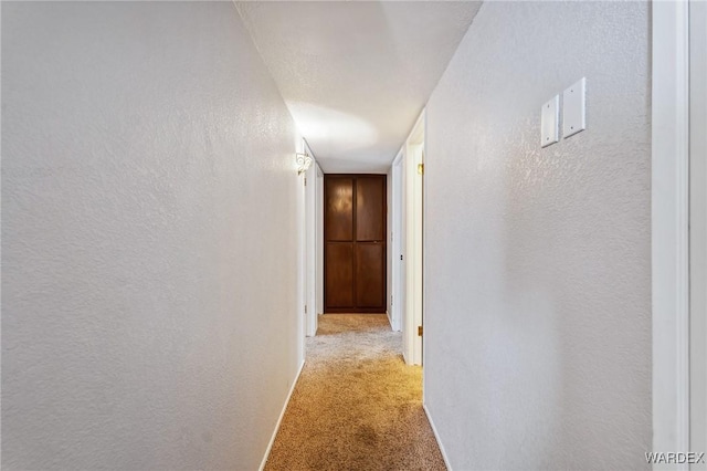 hall featuring light carpet and a textured wall