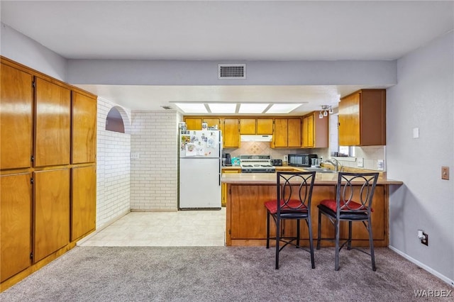 kitchen with a peninsula, stove, brown cabinetry, and freestanding refrigerator