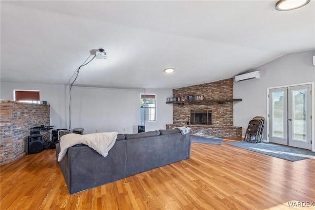 living area with a large fireplace, wood finished floors, vaulted ceiling, an AC wall unit, and french doors