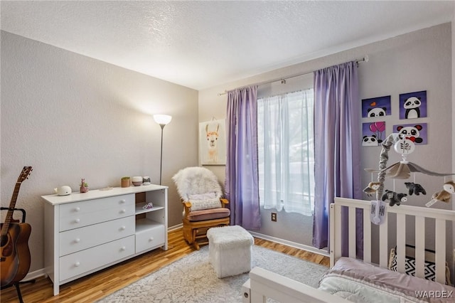 bedroom with a crib, a textured ceiling, baseboards, and wood finished floors