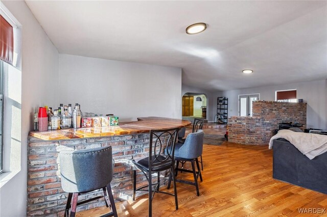 bar with arched walkways, lofted ceiling, a bar, and wood finished floors