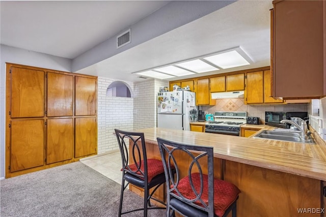 kitchen featuring gas range oven, light countertops, freestanding refrigerator, a sink, and a peninsula