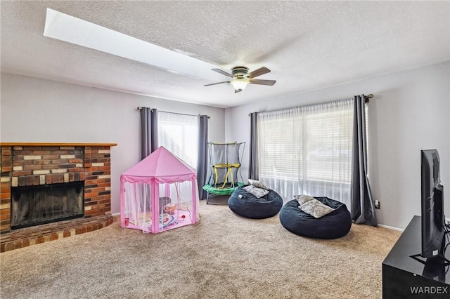 rec room featuring ceiling fan, carpet floors, a textured ceiling, and a brick fireplace