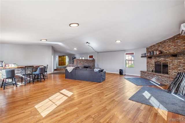 living room with baseboards, lofted ceiling, light wood-style flooring, a brick fireplace, and a wall mounted AC