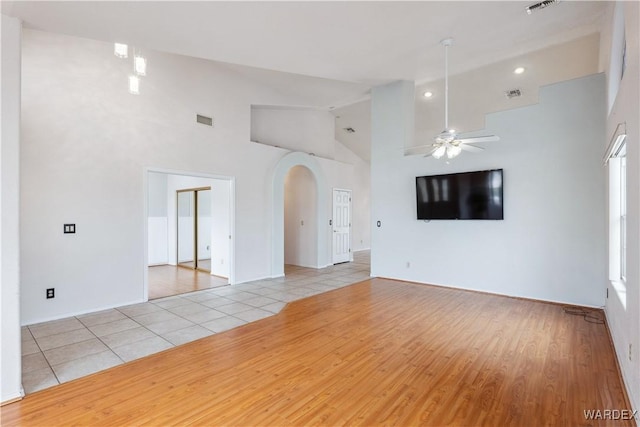 unfurnished living room featuring visible vents, arched walkways, ceiling fan, high vaulted ceiling, and light tile patterned flooring