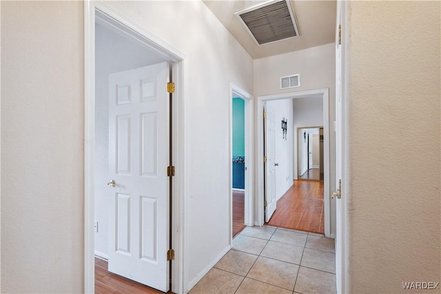 hall with light tile patterned floors, visible vents, and baseboards