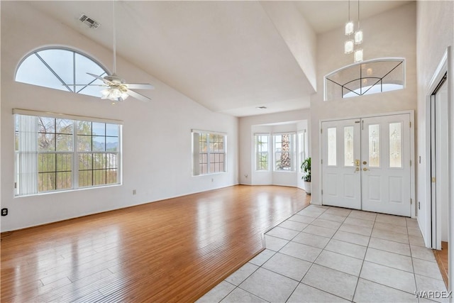 foyer entrance featuring high vaulted ceiling, visible vents, light wood finished floors, and ceiling fan with notable chandelier