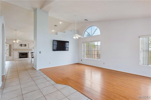 unfurnished living room featuring light tile patterned floors, a fireplace with raised hearth, high vaulted ceiling, and a ceiling fan