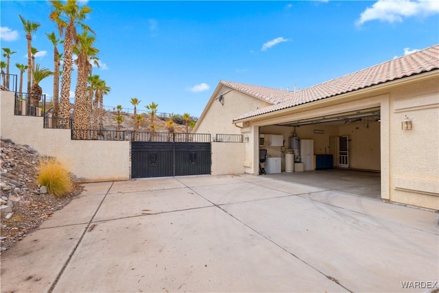 view of home's exterior with an attached garage, concrete driveway, a tiled roof, a gate, and stucco siding