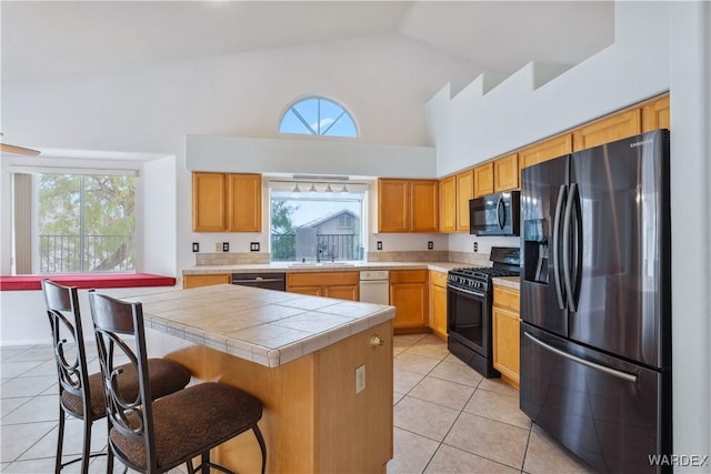 kitchen featuring light tile patterned flooring, a breakfast bar, a sink, a center island, and black appliances