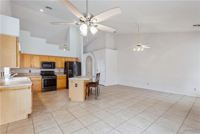 kitchen featuring visible vents, a breakfast bar, open floor plan, black appliances, and a sink