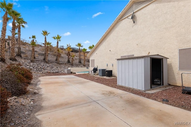 view of side of home with a patio, a fenced backyard, central air condition unit, a shed, and stucco siding