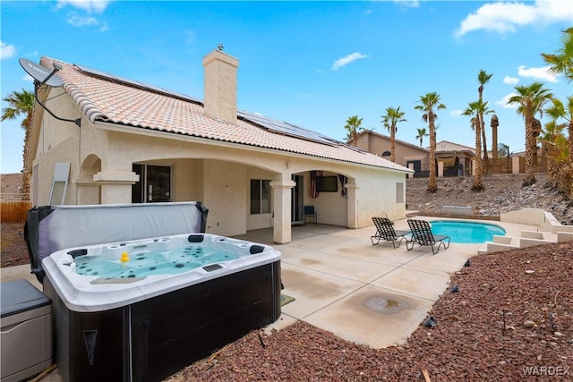 back of house featuring a chimney, stucco siding, a hot tub, a patio area, and a tiled roof