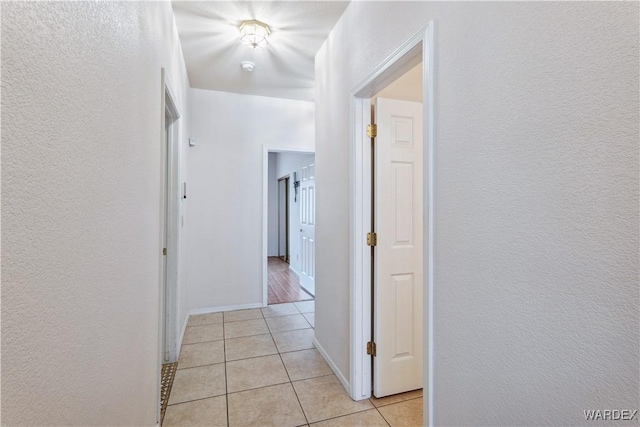 hall with a textured wall, baseboards, and light tile patterned flooring