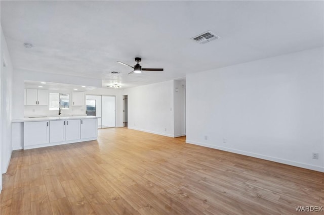 unfurnished living room featuring light wood-style floors, visible vents, baseboards, and a ceiling fan