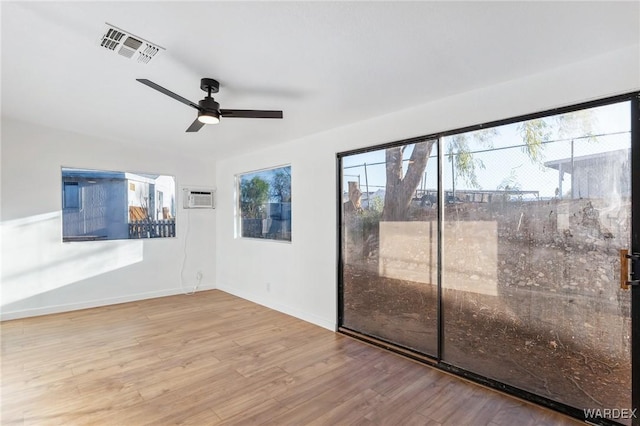 unfurnished room featuring visible vents, a ceiling fan, an AC wall unit, wood finished floors, and baseboards