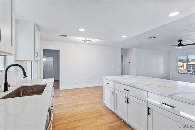 kitchen featuring visible vents, white cabinets, light stone counters, light wood-style floors, and a sink