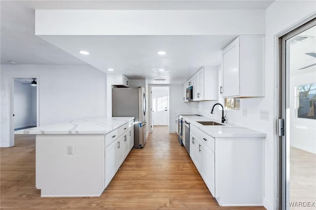 kitchen with appliances with stainless steel finishes, light wood-style floors, white cabinetry, a sink, and light stone countertops