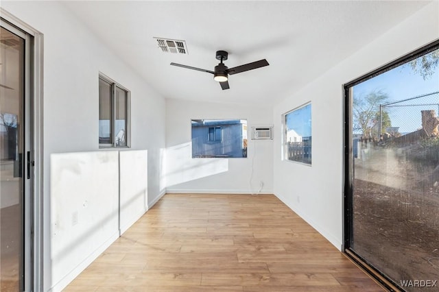 unfurnished room with a wall unit AC, light wood finished floors, visible vents, a ceiling fan, and baseboards