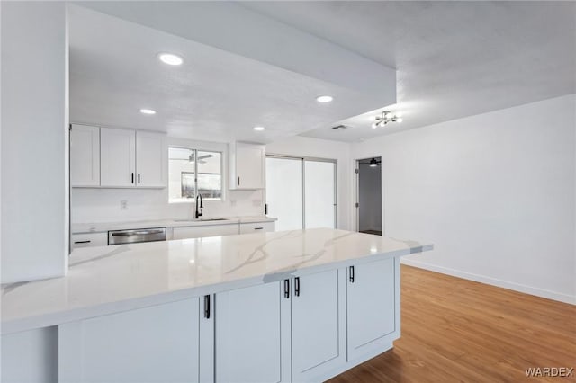 kitchen featuring a peninsula, light wood finished floors, white cabinets, and a sink