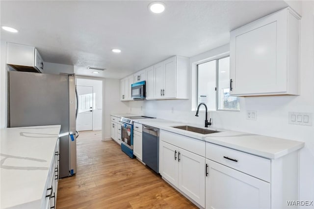 kitchen featuring appliances with stainless steel finishes, light wood-style floors, white cabinetry, and a sink