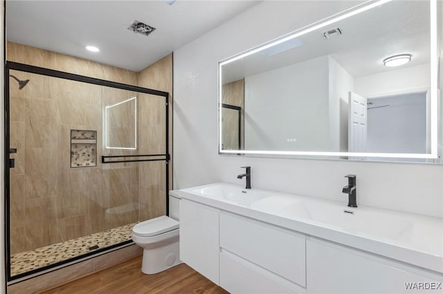 full bath featuring double vanity, visible vents, toilet, wood finished floors, and a sink