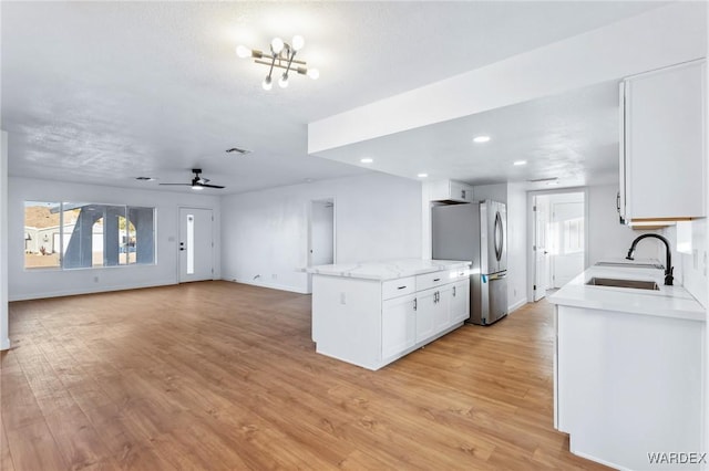 kitchen with light wood finished floors, freestanding refrigerator, open floor plan, white cabinetry, and a sink