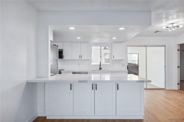 kitchen featuring light wood-style flooring, a peninsula, a sink, white cabinetry, and freestanding refrigerator