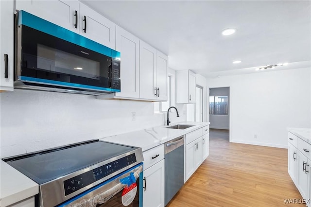 kitchen with light wood-style flooring, light stone counters, stainless steel appliances, white cabinetry, and a sink