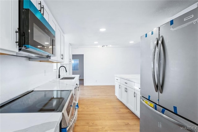 kitchen with appliances with stainless steel finishes, white cabinetry, a sink, and light stone countertops