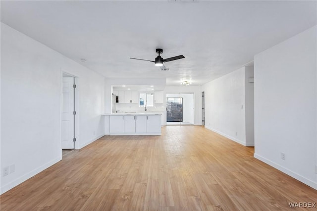 unfurnished living room with light wood-type flooring, a sink, a ceiling fan, and baseboards