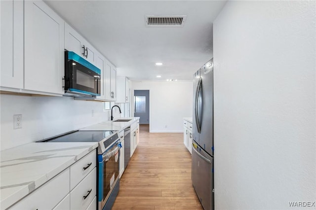 kitchen featuring light stone counters, visible vents, appliances with stainless steel finishes, white cabinets, and a sink