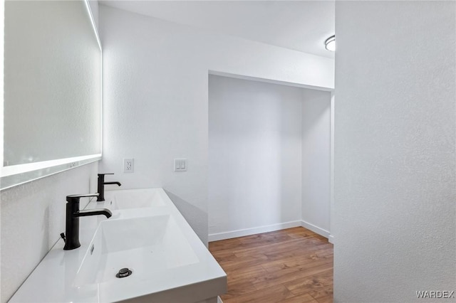 bathroom with a sink, double vanity, wood finished floors, and baseboards