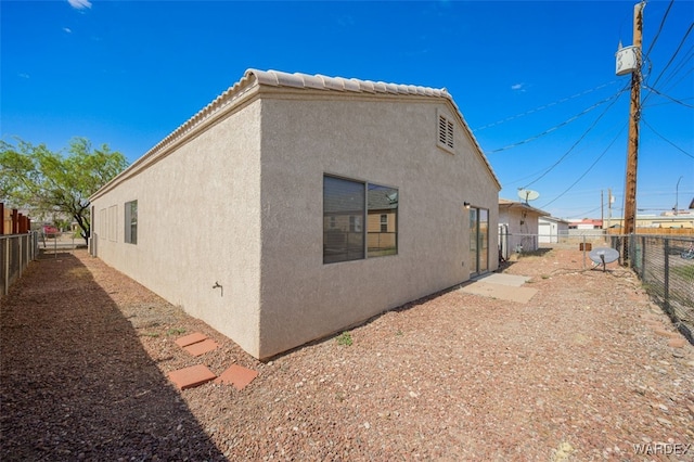 view of side of home featuring a tile roof, fence, and stucco siding