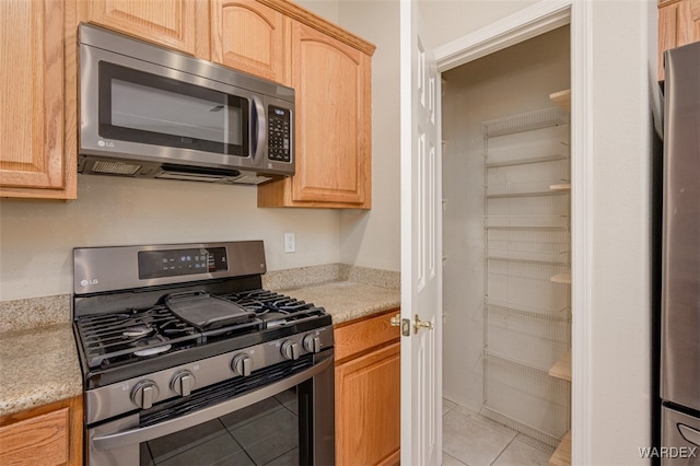 kitchen with light brown cabinetry, appliances with stainless steel finishes, and light tile patterned flooring