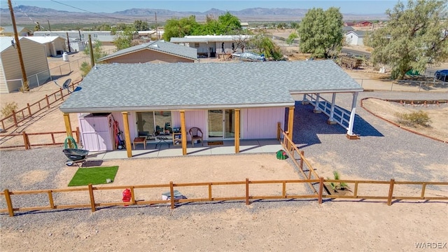 rear view of property featuring roof with shingles, an outdoor structure, fence, and a mountain view