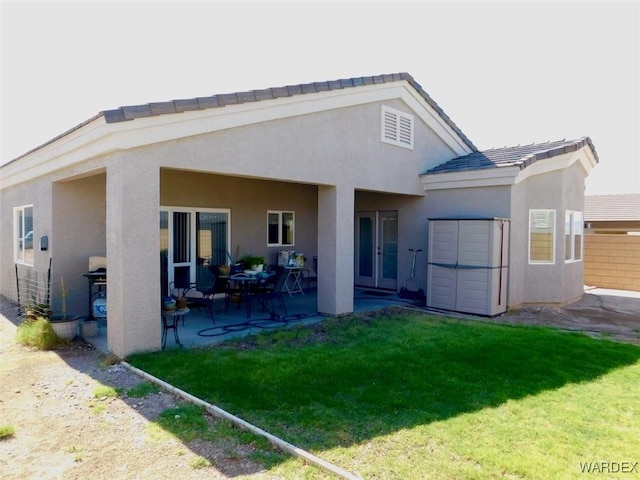 rear view of house with a patio area, a lawn, fence, and stucco siding