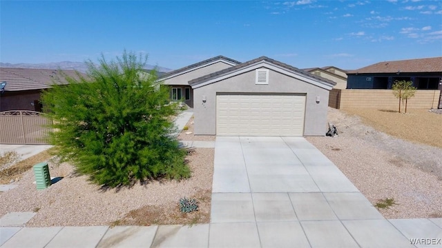 ranch-style house featuring an attached garage, a mountain view, fence, driveway, and stucco siding