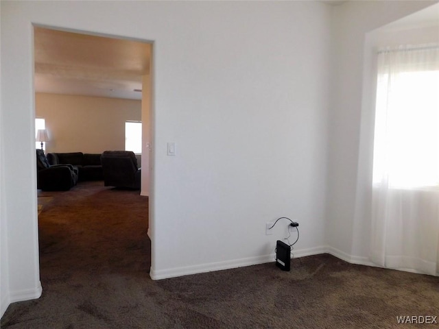 unfurnished room featuring plenty of natural light, dark carpet, and baseboards