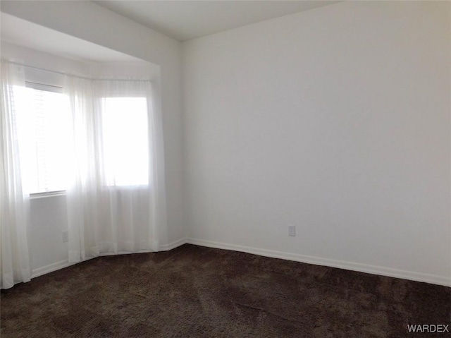 spare room featuring dark colored carpet and baseboards