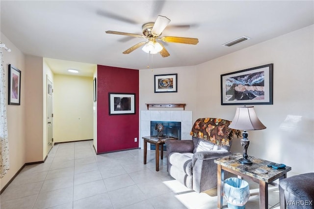 living room with light tile patterned floors, visible vents, baseboards, a tile fireplace, and ceiling fan