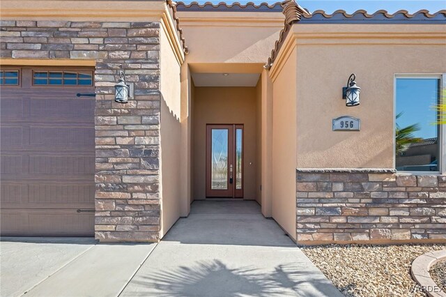 property entrance with a garage, stone siding, a tile roof, and stucco siding