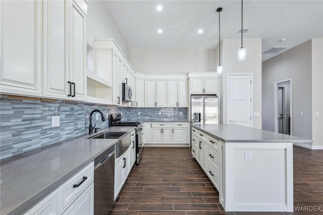 kitchen with stainless steel appliances, wood finish floors, a kitchen island, white cabinets, and decorative light fixtures