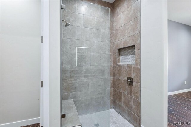 full bath with baseboards, a tile shower, and wood finished floors