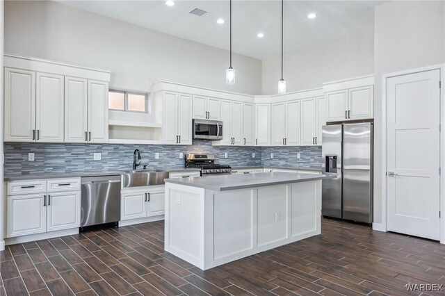 kitchen featuring appliances with stainless steel finishes, a center island, hanging light fixtures, light countertops, and a sink