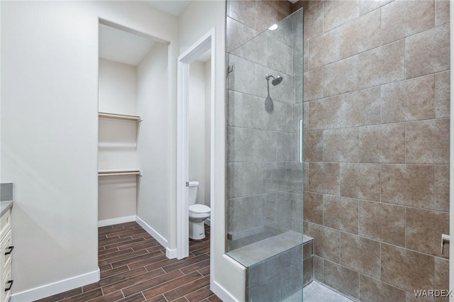 bathroom featuring a spacious closet, toilet, wood tiled floor, vanity, and walk in shower