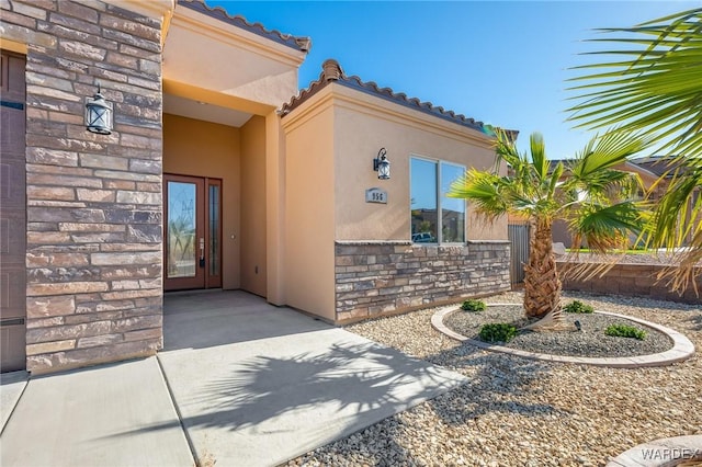 view of exterior entry featuring stone siding, a patio, a tiled roof, and stucco siding