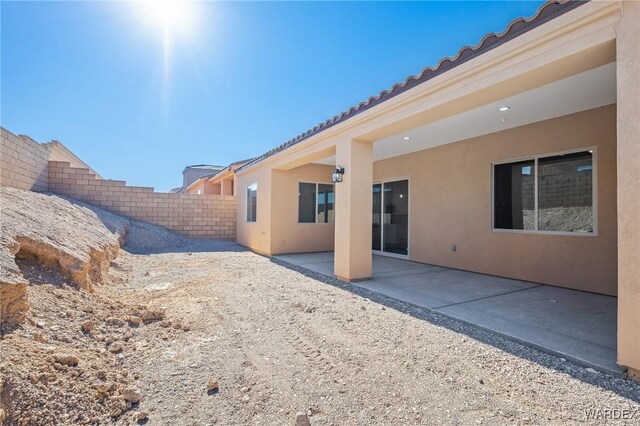 rear view of property featuring a tile roof, a patio area, fence, and stucco siding