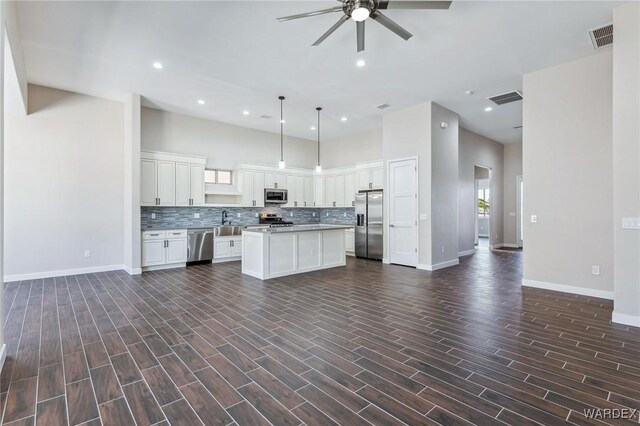 kitchen featuring white cabinets, appliances with stainless steel finishes, decorative light fixtures, a center island, and a sink