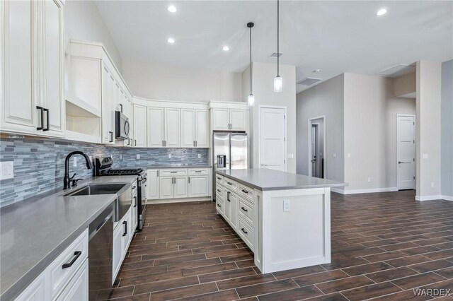 kitchen with a center island, wood finish floors, decorative light fixtures, stainless steel appliances, and white cabinetry